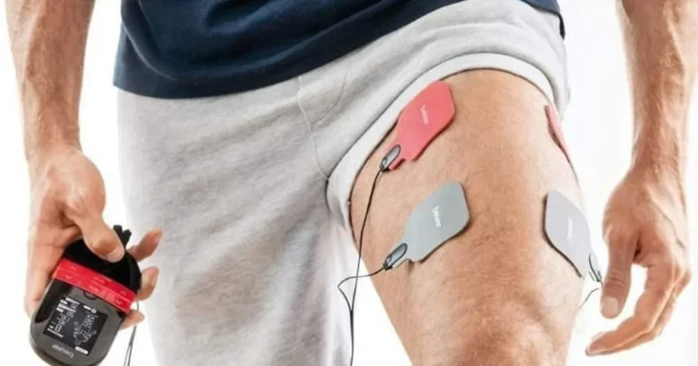 Mężczyzna trzyma elektrostymulator Beurer EM 59, a na jego udzie są przyklejone cztery elektrody