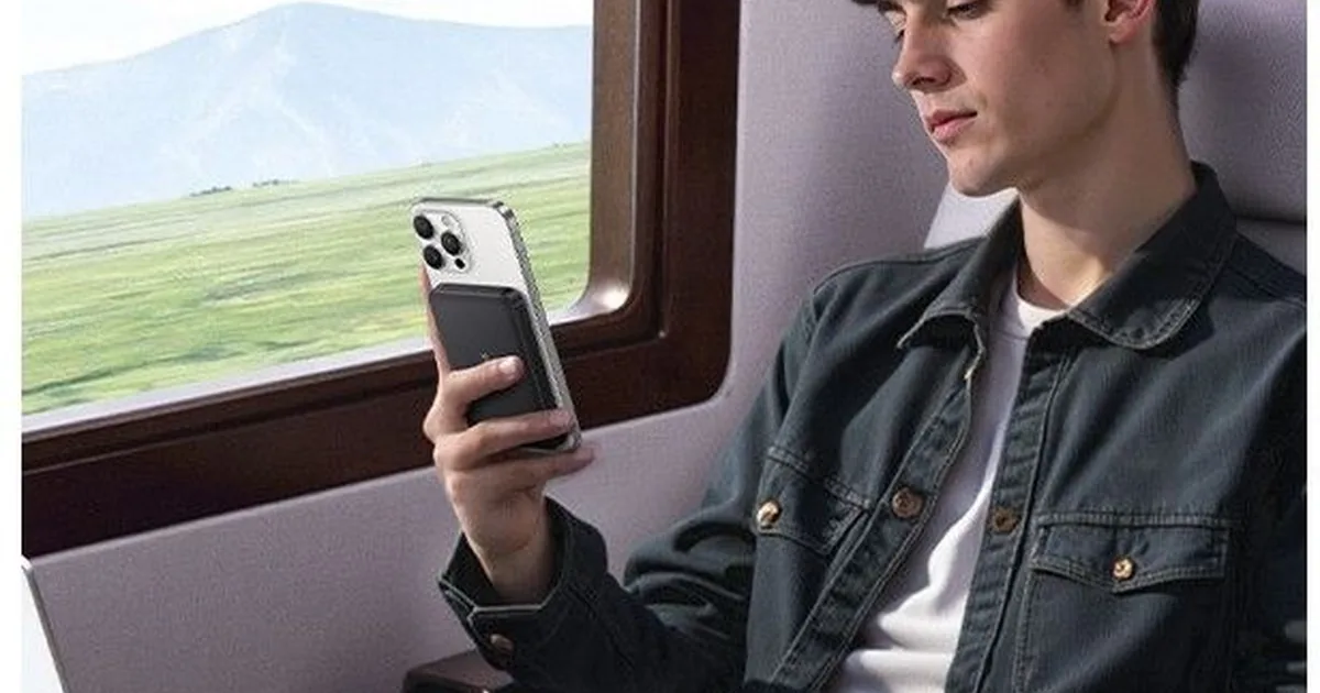 Mężczyzna w pociągu trzyma iPhone’a z przyczepionym magnetycznie powerbankiem Baseus